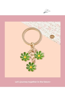 Detail of golden metal keychain featuring three green enamel daisy flower charms