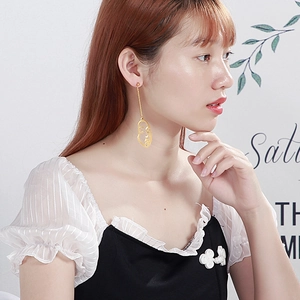 Boucles d'oreilles pendantes visage abstrait doré portées par un mannequin de style épuré