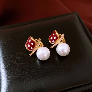 Macro shot of gold-plated earrings with red geometric patterns and hanging white pearls