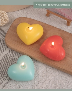 Three colorful heart-shaped scented candles in yellow, red, and blue on a wooden tray