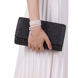 Close-up of a black woven straw clutch bag texture held by a hand with beaded bracelet