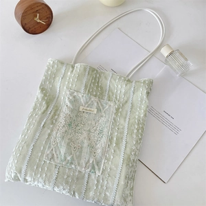 Detail of light green lace tote bag showing delicate embroidery on a white desk