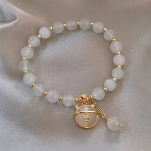 Elegant Lucky Cat charm bracelet with white jade beads and golden bells on silk fabric