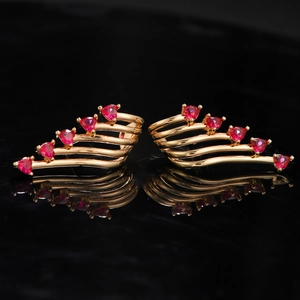 Detail of gold-plated wing earrings featuring red heart-shaped crystals on black backdrop