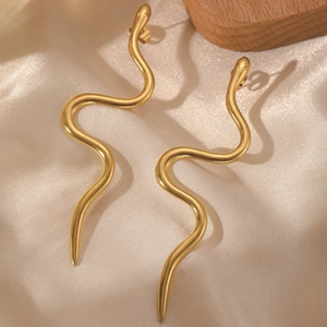 Detailed view of polished gold snake-shaped curved earrings on a beige satin surface