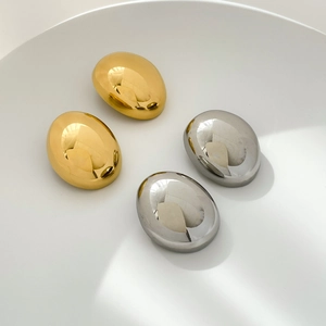 Polished gold and silver oval drop earrings with mirror finish on white display