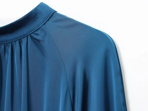 Detailed close-up of dark blue silk-satin dress showing turtleneck pleats and shoulder seams