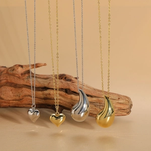 Polished silver and gold minimalist heart and teardrop pendant necklaces on wood