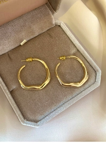 Close-up of golden irregular wavy hoop earrings displayed in a velvet jewelry box