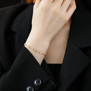 Detail of a gold-plated bracelet featuring five diamond-set flowers on a delicate chain