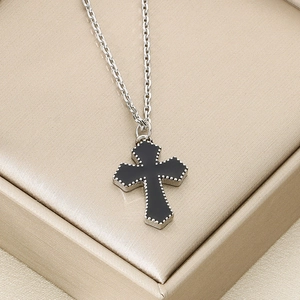 Macro detail of silver cross pendant with black filling on golden silk background