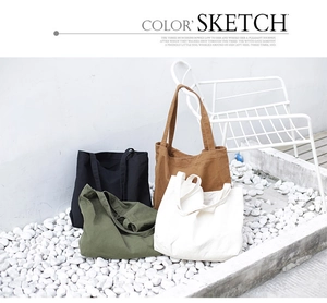 Minimalist canvas tote bags in black, caramel, green, and white on pebble stone floor