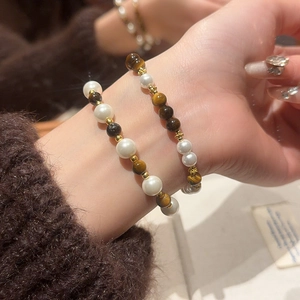 Detailed view of layered tiger eye and pearl beaded bracelets on a wrist