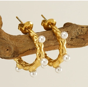 Détail de boucles d'oreilles C dorées avec texture lave et perles sur une branche