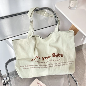 Close-up of light green canvas tote bag with brown lettering on a minimalist chair