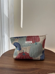 Detailed close-up of a pumpkin pattern fabric cosmetic bag on a wooden display stand