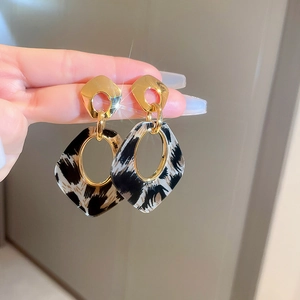 Détail de boucles d'oreilles géométriques dorées avec des breloques à motif léopard
