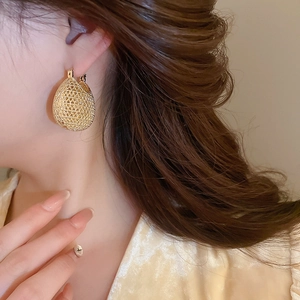 Close-up of golden teardrop hollow mesh earrings worn by a model in warm lighting