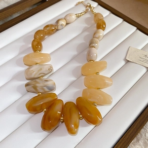 Detail view of acrylic beaded necklace with amber and marble resin beads on white tray