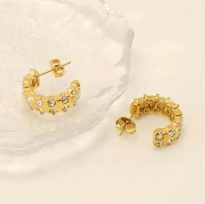 Detailed macro shot of C-shaped gold earrings with double-row crystals on glass texture