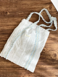 Sac fourre-tout en dentelle blanche avec bordures à franges bleues sur fond de bois