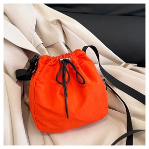 Detail of orange drawstring bucket bag with black wide strap on beige trench coat