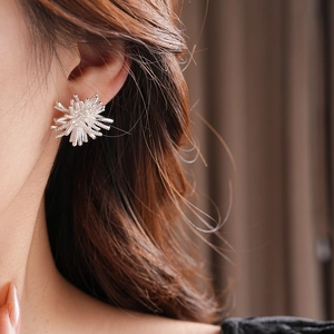 Close-up of silver-tone radial firework stud earrings worn by a model in a luxury setting