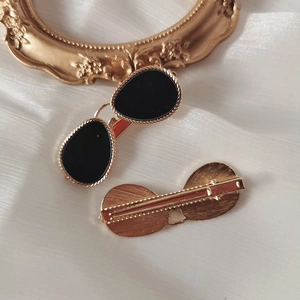 Elegant gold metal glasses-shaped hair clips with black oval detail on silk fabric