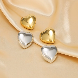 Polished heart earrings in gold and silver finish on elegant silk fabric background