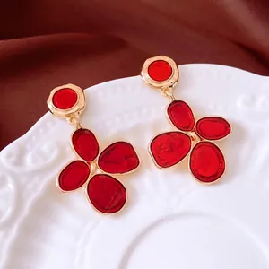 Vintage gold-plated floral earrings with red resin petals on an elegant ceramic plate