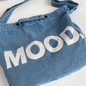 Retro denim tote bag with white MOOD lettering and snap closure on white background