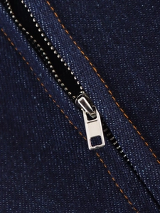 Close-up of dark blue denim fabric with silver metal zipper and orange stitching detail