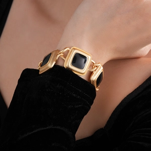 Close-up of a vintage golden wide bracelet with black square gemstones on a wrist