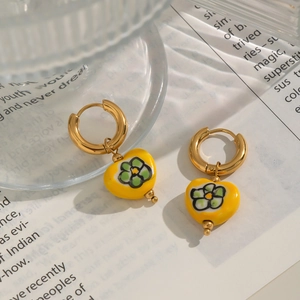 Gros plan de boucles d'oreilles cœur jaunes avec motif floral vert et créoles dorées