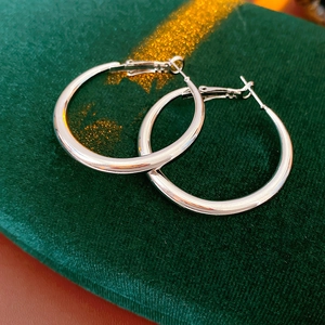 Close-up of minimalist silver U-shaped hoop earrings on dark green velvet surface