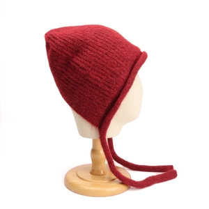 Dettaglio del cappello in maglia rosso scuro con paraorecchie e lunghi nastri decorativi