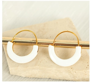 Detail view of gold hoop earrings with white enamel charms on a minimalist stone display