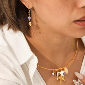 Detail of nautical gold necklace and earrings with ceramic beads and pearls on a model