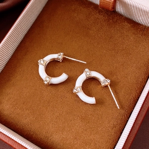 Macro view of white enamel bamboo-style C-shaped earrings with gold diamond-set accents