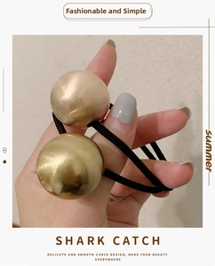 Detail of high-elastic black hair tie with two large brushed gold metallic sphere accents
