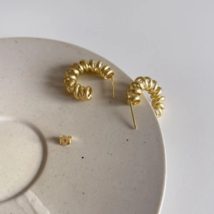 Macro shot of gold spiral spring earrings displayed on a textured ceramic plate