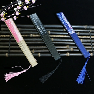 Three elegant Chinese folding fans in pink, black, and blue silk on a dark bamboo mat