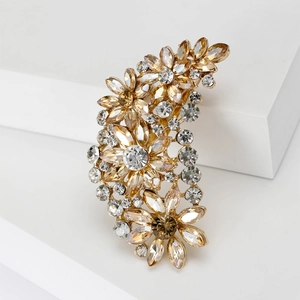 Detailed close-up of golden floral brooch with amber and champagne crystals on white block