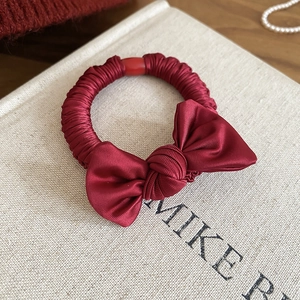 Close-up of wine red satin bow scrunchie with silk texture on a neutral background
