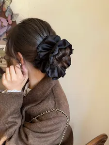 Detailed shot of a large black satin scrunchie with elegant pleated fabric texture
