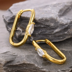 Macro view of gold oval hoop earrings with marquise zircon on a grey stone background