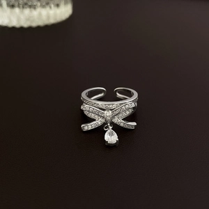 Close-up of silver bow ring with micro-pave crystals and a hanging pear-shaped gemstone