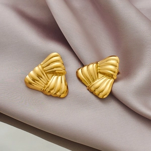 Détail macro de boucles d'oreilles triangulaires dorées sur tissu de soie argenté