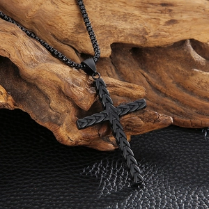 Detail of black stainless steel cross pendant with a woven texture on rustic wood