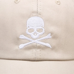 Close-up of precise white skull embroidery on a beige cotton twill baseball cap